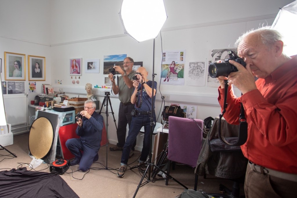 4 older men take photos within an art studio. They are surrounded by photographic lighting equipment.